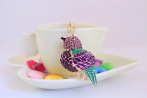 Detailed view of bird keychain with purple rhinestones and green enamel wings