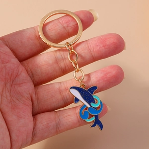 Détail d'un porte-clés dauphin en émail bleu avec accents dorés tenu dans la main