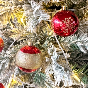 Close-up of red and gold Christmas balls with snowflake patterns on a snowy tree