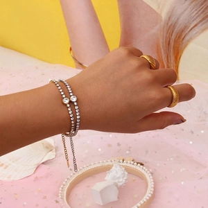 Minimalist round zircon bracelets and textured gold rings set on female model's hand