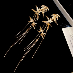 Detailed close-up of golden bamboo leaf tassel earrings on elegant black velvet background