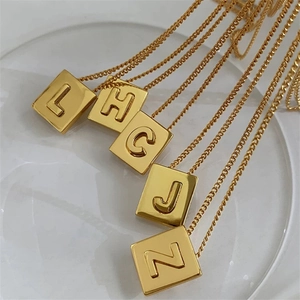 Detailed view of square gold initial pendants L, H, C, J, Z on a glass jewelry tray