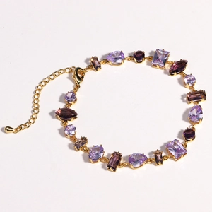 Elegant gold bracelet with blue zircon and purple crystals on a clean white background
