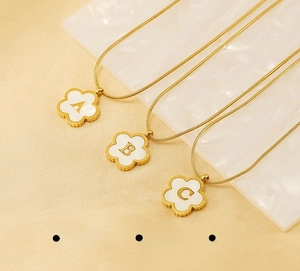 Macro detail of 18K gold plated clover necklaces with white shell alphabet pendants