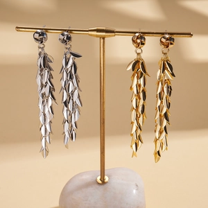 Golden and silver geometric leaf tassel earrings hanging on a minimalist display stand