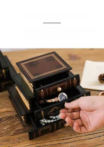 Three-layer vintage faux book jewelry box storing watches and necklaces on a wooden desk