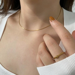 Detail of a thin gold snake chain necklace and beaded ring styled on a model