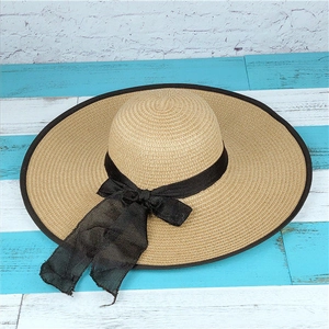 Detailed view of wide brim straw hat with woven texture and a black ribbon bow decoration