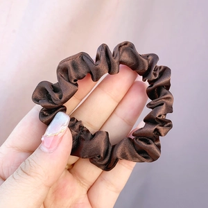 Detail of dark brown satin scrunchie with soft pleated texture and elastic stretch