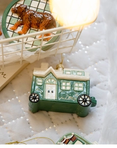 Detail shot of a vintage green Christmas house pendant on a white sequin fabric background