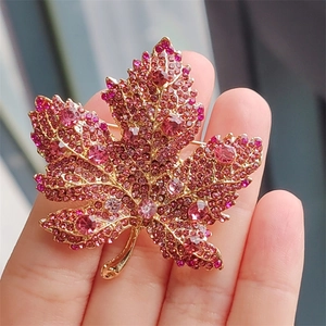 Close-up of pink maple leaf brooch with sparkling crystals held in hand for scale