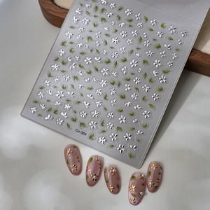 3D floral nail stickers with silver flowers and green leaves on minimalist background