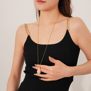 Detail of a textured golden pear-shaped pendant on a long beaded chain worn by a model