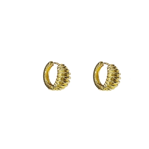 Détail de boucles d'oreilles créoles dorées avec texture géométrique côtelée