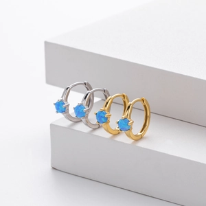 Close-up of gold and silver S925 huggie earrings featuring round blue opal stones