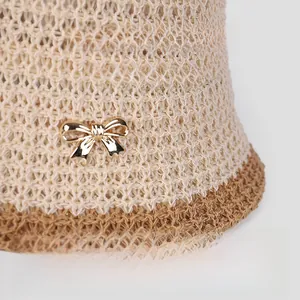 Detail of breathable knitted bucket hat featuring a gold bow and brown contrast trim