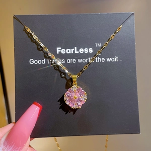 Macro detail of pink flower pendant with cubic zirconia and gold chain on black card