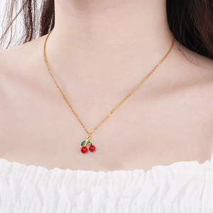 Close-up of a gold cherry pendant necklace with red fruit and green leaves on a model