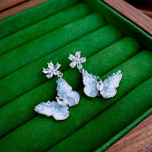 Detailed macro view of light blue stone butterfly earrings on a green velvet box