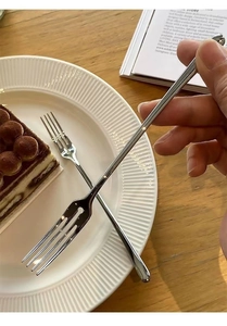 Elegant stainless steel dessert fork held by hand over a delicious cake on a white plate