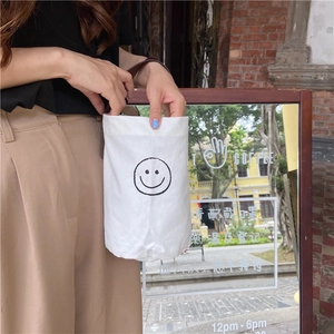 Detail of white canvas bucket bag featuring a black smiley face and dark handles