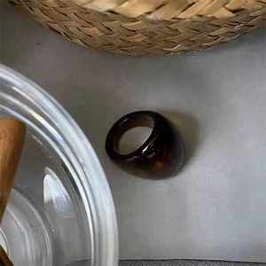 Detailed close-up of wide amber resin ring with retro geometric texture on a woven surface