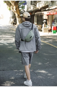 Outdoor street view of a pale green nylon sling bag with adjustable strap worn as a waist pack