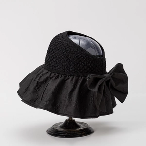 Detail of black hollow top sun hat with large bow and floral pattern brim on a stand
