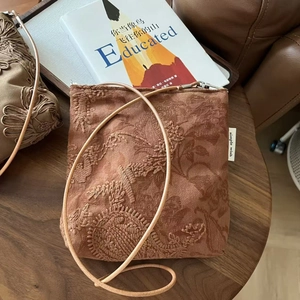 Détail de la broderie florale sur le sac bandoulière en suédine camel avec étiquette