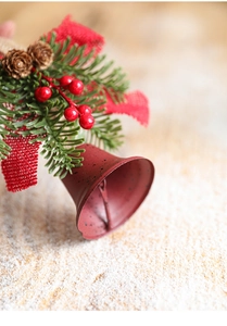 Detail of red metal bell with pine branches, red berries, and bow for Christmas decor