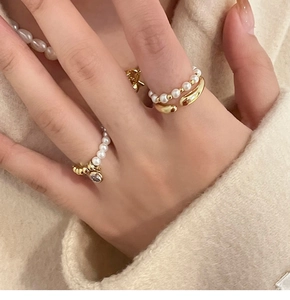 Gros plan d'un ensemble de bagues et collier en perles dorées sur un pull en maille beige