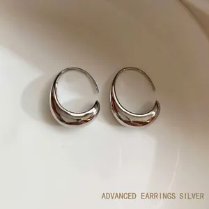Macro shot of polished silver drop earrings on white surface with a sleek mirror finish