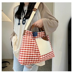 Detail view of red checkered canvas tote bag with beige pocket and brown leather handles