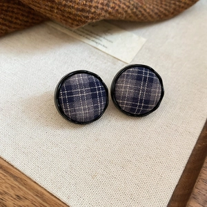 Close-up of retro navy blue plaid fabric earrings on a soft textured background