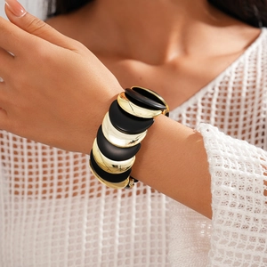 Primo piano di un bracciale in acrilico nero e oro con design geometrico semicircolare al polso