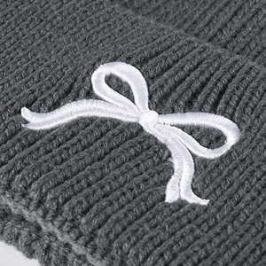 Deep grey knit beanie with white bow embroidery and thick ribbed texture detail