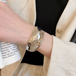 Gros plan d'un large bracelet manchette argenté poli porté sur une manche de blazer