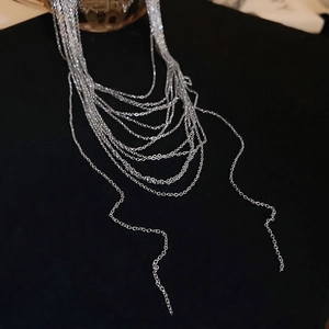 Dettaglio macro di una collana a strati d'argento minimalista drappeggiata su fondo nero