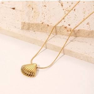 Detailed view of a gold shell pendant on a fine chain over a textured stone surface