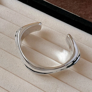 Polished silver irregular wave cuff bracelet displayed on a premium cream velvet tray