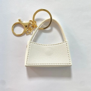 Dettaglio portachiavi mini borsa in pelle bianca con accessori dorati e chiusura a scatto