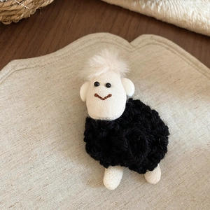 Close-up of handmade sheep plush brooch with black knitted body and cute white face