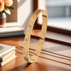 Detalle de brazalete de acero inoxidable oro 18K con grabados de ojos y cristales de color