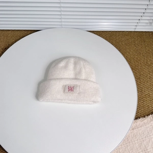 Close-up of white knitted wool beanie with BAKE label on textured background