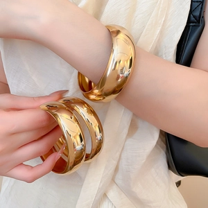 Gros plan sur un ensemble de larges bracelets en métal doré poli au fini miroir lisse