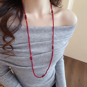 Close-up of long red beaded necklace with gold spacer beads on a grey sweater