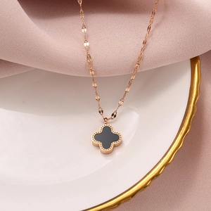 Macro shot of rose gold four-leaf clover necklace on white porcelain and pink silk