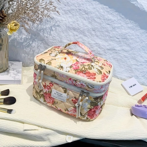 Floral quilted cosmetic bag with top handle and dual zippers on white fabric background