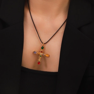 Detail of gold cross necklace with colorful gemstones worn with a black blazer