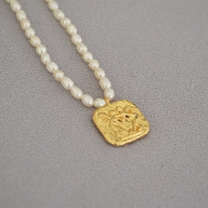 Detail shot of white freshwater pearls and golden coin pendant with vintage relief